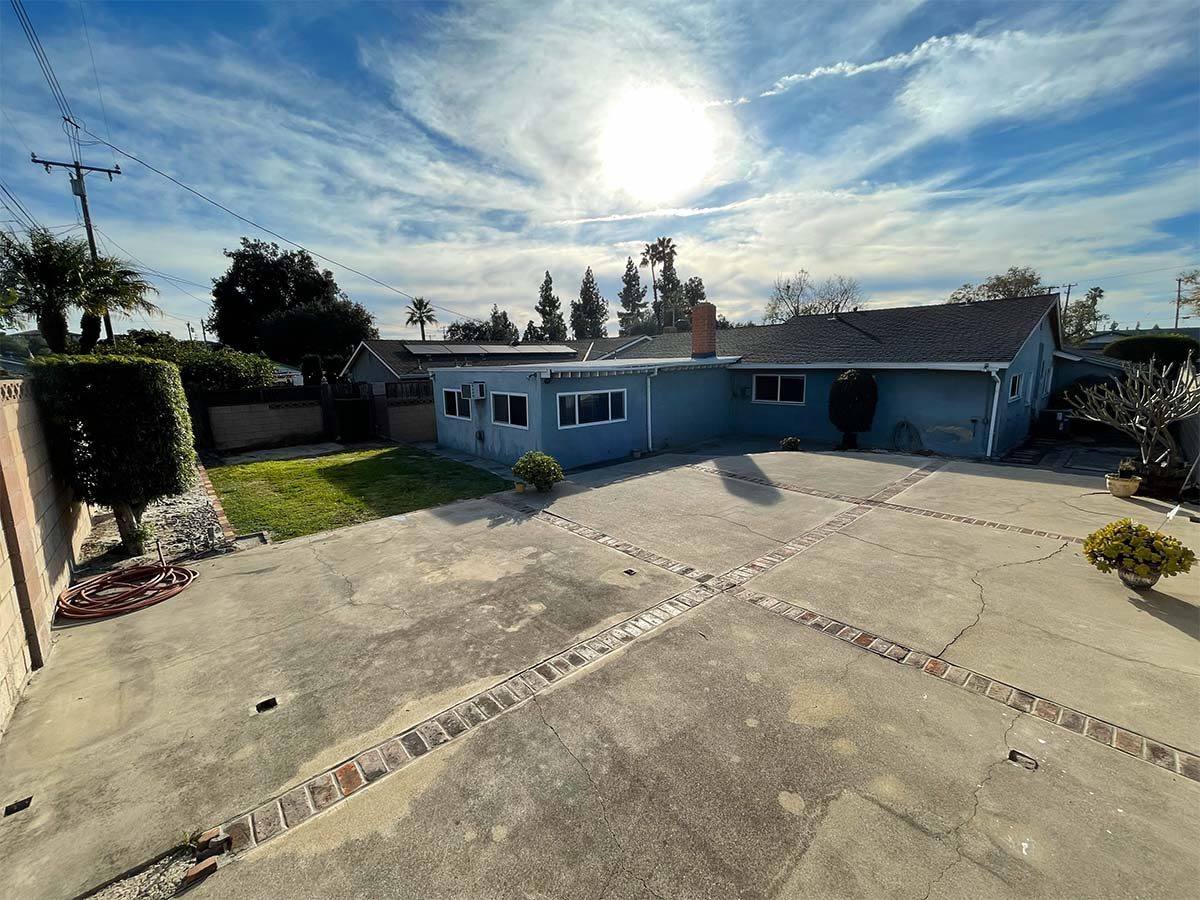 Backyard of 514 N Balton Ave, San Dimas, with a grass lawn, block wall fencing, mature hedges and a large open concrete patio on the 7,410 square foot lot